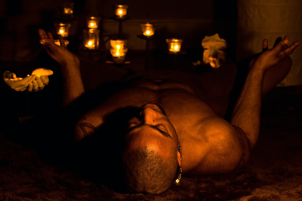 A Shirtless Man Lying on the Ground among Burning Candles
